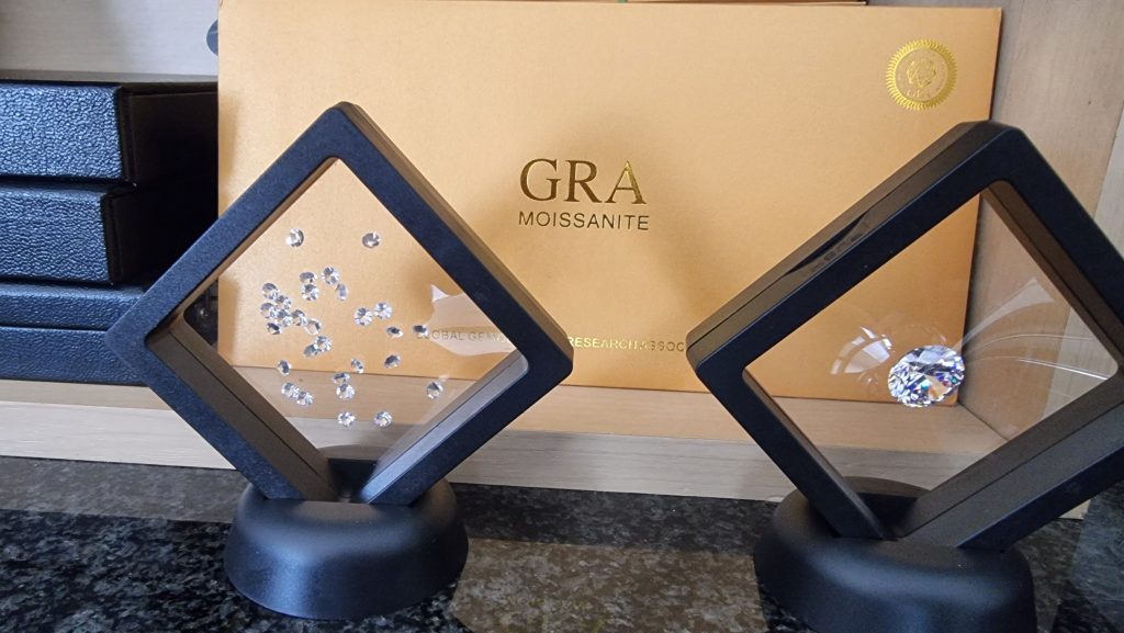 Elegant display of various sizes of sparkling moissanite stones in black geometric stands with a golden GRA Moissanite certification card in the background, highlighting the gem's premium quality.