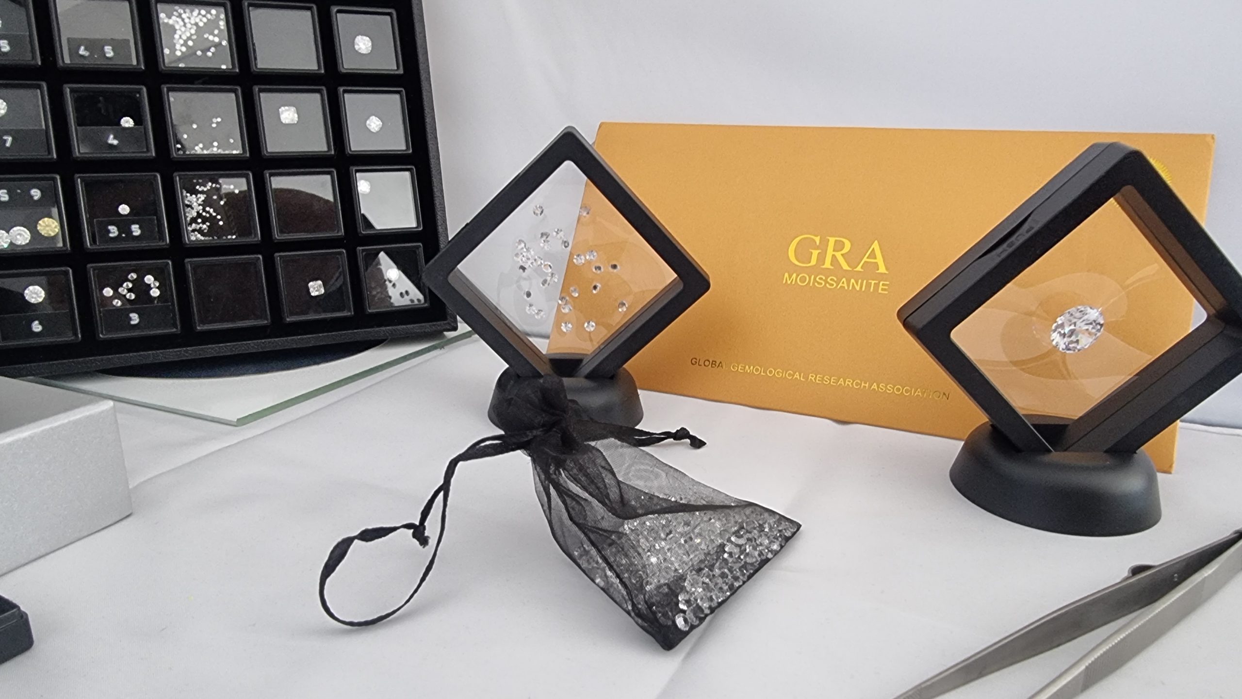 A professional moissanite display at a jeweler's showcasing various cuts and sizes of moissanite stones, with a prominent GRA Moissanite certification in the background.