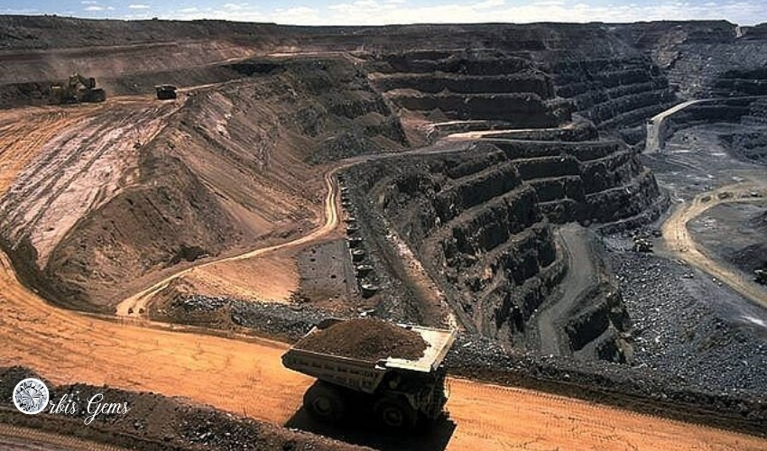 An expansive open-pit diamond mine with heavy machinery, underscoring the environmental impact argument that moissanite is better than diamond.